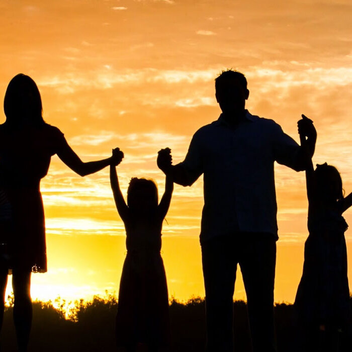 A family is standing in the sunset with their hands raised.